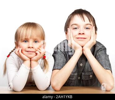 Portrait of cute girl and boy sitting at desk with hands on chin Stock Photo