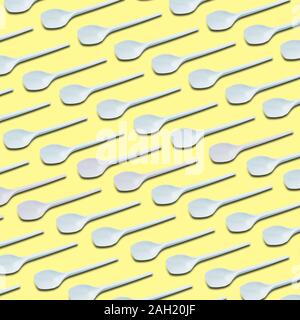 white plastic tea spoons pattern on yellow background Stock Photo