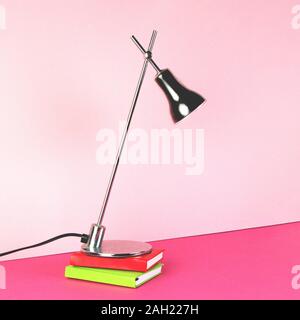 A metal table lamp stands on two notebooks on a pink background. Stock Photo