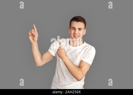 Copy Space for Text or Product. Young man standing isolated on grey pointing up joyful Stock Photo
