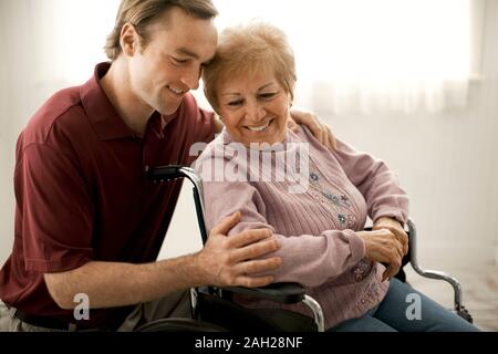 Smiling senior woman talking with a male nurse and being comforted while sitting in a wheelchair. Stock Photo