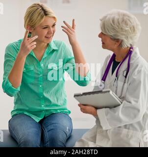 Happy young woman explaining to a female doctor while sitting together side by side inside a doctor's office. Stock Photo