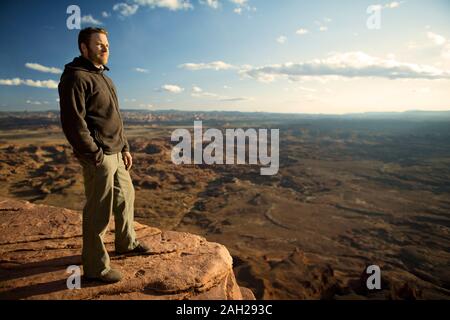 Mid adult man standing on top of a rock formation overlooking a canyon Stock Photo