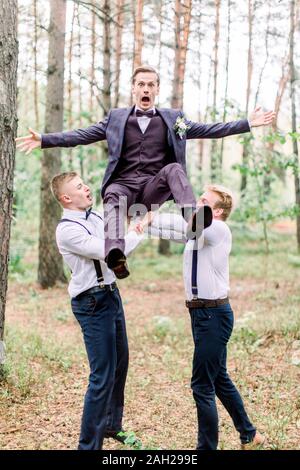 Stylish groom and groomsmen having fun in the forest. Groom is jumping up with crazy funny face. Stock Photo