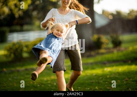 Mid adult woman playfully spinning her happy young daughter around in the backyard Stock Photo