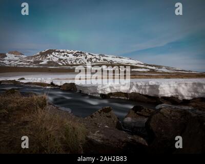 Long exposure of icelandic glacier at night with river in foreground and northern lights slightly visible. Winter shot with different layers of snow a Stock Photo