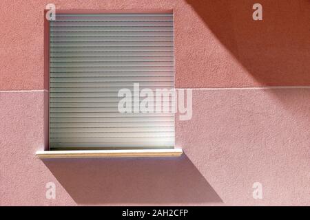 Minimalist blue window with shadow from the sun on a wall. A square red window hanging on a side wall of building Stock Photo