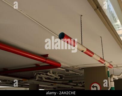 Closeup car height restriction sign made from PVC pipe painted with red and white, hanging from ceiling by chains at parking lot entrance Stock Photo