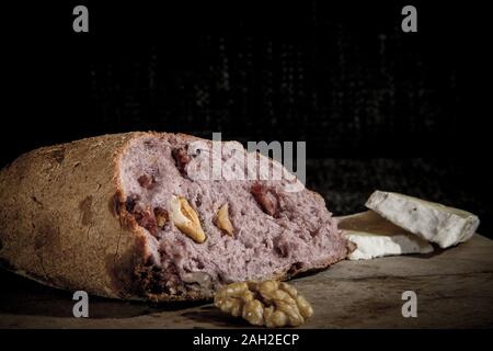 Wine flavoured bread (pain au vin) with its typical red inside, stuffed with walnuts, on display on a wooden plank, next to slices of Brie fromage che Stock Photo
