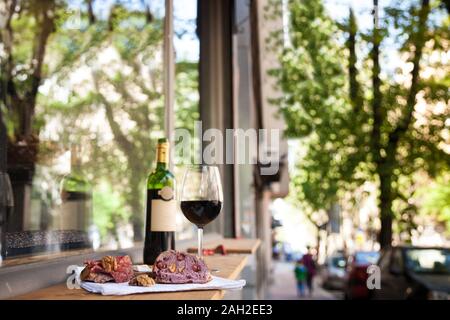 slices of baguette bread, brie cheese and saucisson (a cured meat from France) for appetizers with a Glass and bottle of French red wine, blurred in t Stock Photo