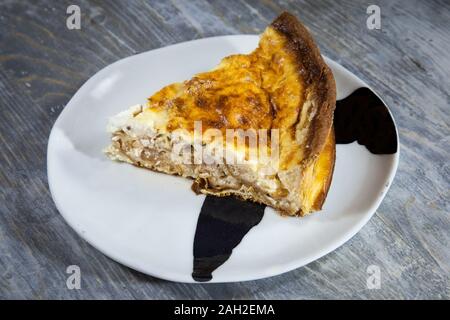 Close up on a slice cut of a Traditional French Quiche Lorraine pie on display on a plate on a rustic wooden table. It is an iconic dish of Eastern Fr Stock Photo