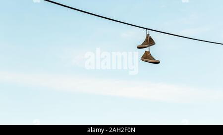 Pair of old shoes or sneakers hanging from a power line by the laces Stock Photo