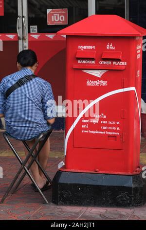 A lottery vendor sitting in front of a post office next to a red letter-box in Bangkok, Thailand Stock Photo