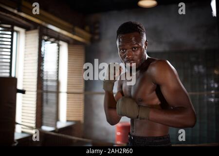 Portrait of African young muscular man standing and posing at camera while training in gym