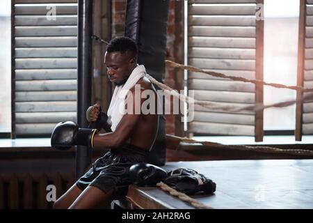 African muscular boxer sitting near the boxing ring wearing boxing gloves he preparing for fight