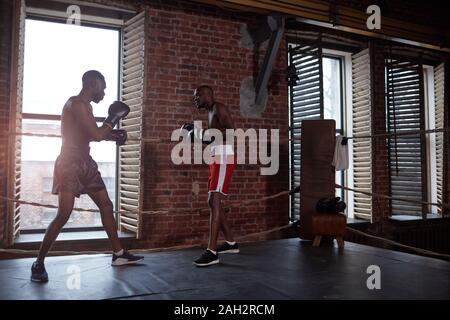 Two African boxers in sports clothing fighting with each other on boxing ring in the gym Stock Photo