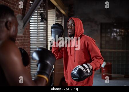 Two African sportsmen wearing boxing gloves and practicing fight during sports training in gym Stock Photo
