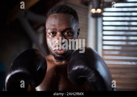 Portrait of African young sportsman in boxing gloves looking at camera during training in gym Stock Photo