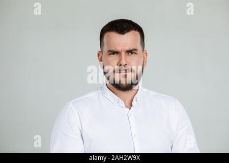 Portrait of young frowned handsome bearded man on gray background. facial expression Stock Photo