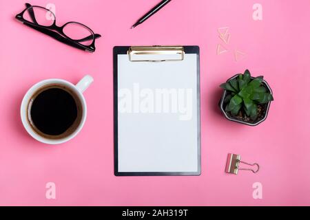 Clipboard with blank paper on the pink table with coffee, glasses and succulent plant, top view Stock Photo