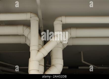 Closeup row of large plastic water pipes painted with white color run under ceiling of a building, selective focus Stock Photo