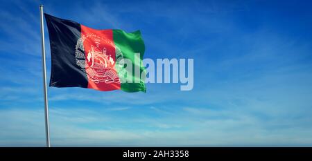 The National flag of Afghanistan blowing in the wind in front of a clear blue sky Stock Photo