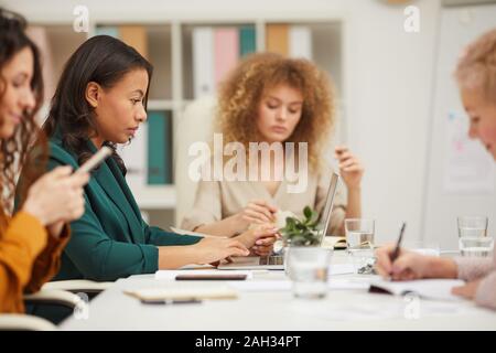 Group of four successful women sitting together at table in board room doing their job horizontal eye level shot Stock Photo