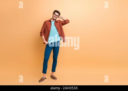 Full length body size view of his he nice attractive fashionable cheerful cheery brunet guy macho hipster posing touching hair isolated over beige Stock Photo