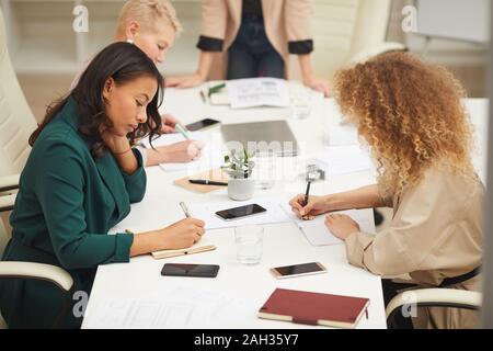 Group of creative businesswomen brainstorming at meeting writing down their ideas in notebooks, horizontal high angle shot Stock Photo