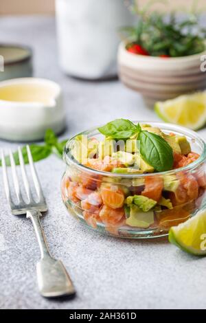 Delicious avocado and raw salmon salad, tartare, served glass jar with lime, light background Stock Photo