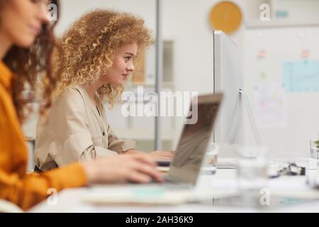 Two young women with curly hair working on modern computers in office side view shot Stock Photo