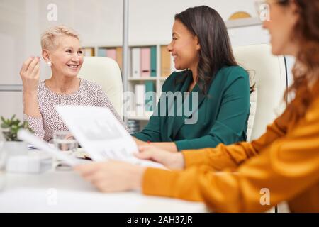 Three cheerful businesswomen of chatting while sitting at office table working together Stock Photo
