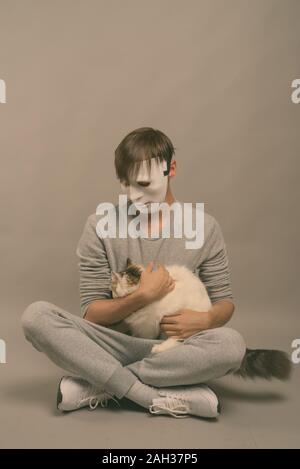Studio shot of young man wearing white mask while holding cute cat against gray background Stock Photo