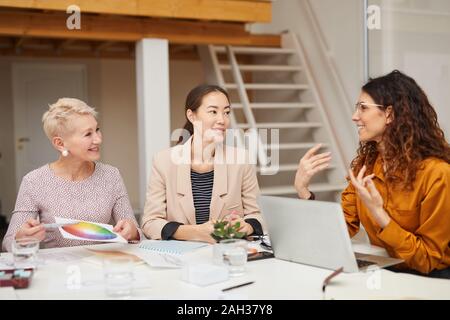 Three stylish clothes designers sitting together in office room having discussion on new collection issue Stock Photo