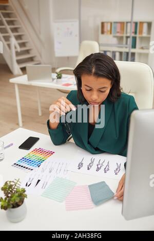 Vertical high angle portrait of concentrated young woman working on new clothes collection concept in office alone Stock Photo