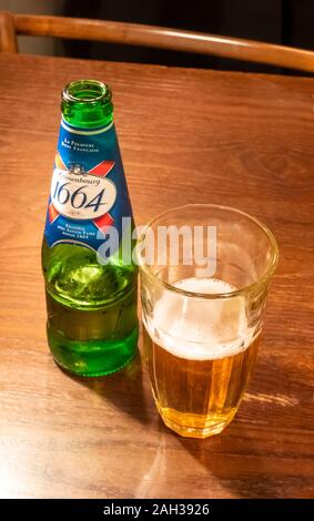 Open bottle of Kronenbourg 1664 lager beer beside a half-full glass Stock Photo