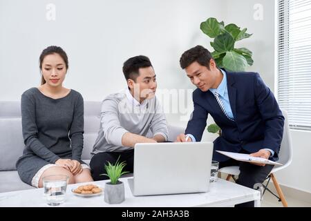 It is not my fault! Displeased young man talking to psychiatrist and gesturing while his wife sitting near him and keeping arms crossed Stock Photo