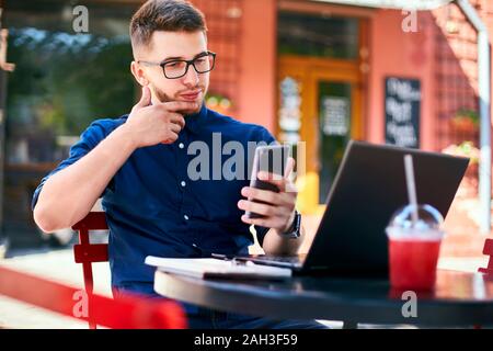 Successful businessman holding mobile modern smartphone. Happy hipster with a modern phone enjoys pleasant news. Smiling young man in glasses with lap Stock Photo