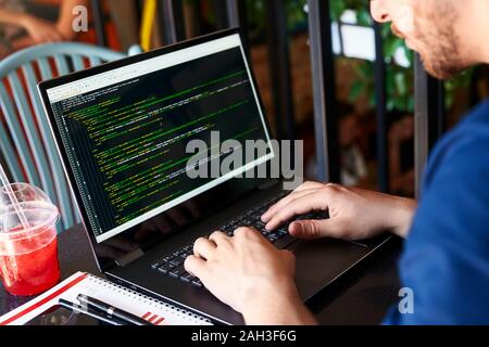 Back view over the shoulder shot of developer programmer with laptop. Program code and script data on the screen. Young freelancer in glasses working Stock Photo