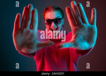 Framing. Caucasian woman's portrait isolated on gradient studio background in neon light. Beautiful female model with sunglasses, red hair. Concept of human emotions, facial expression, ad. Stock Photo