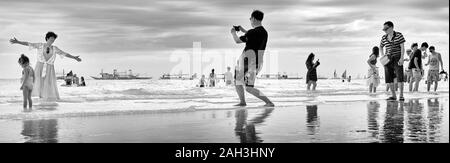 Boracay, Aklan Province, Philippines - January 6 2018: Group of Chinese tourists walking along White Beach, husband is taking pictures of posing wife. Stock Photo