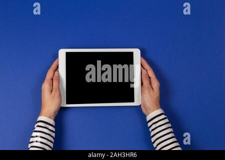 Female hands holding digital tablet computer on navy blue background. Top view Stock Photo