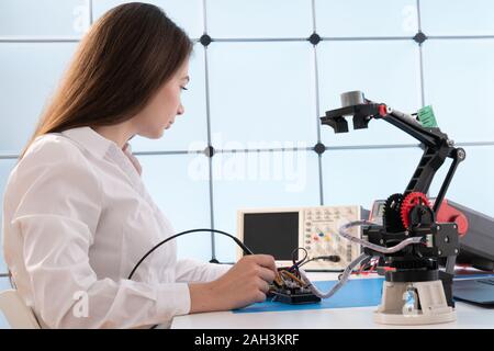 A young woman writes an algorithm for the robot arm. Science Research Laboratory for Robotic Arm Model. Computer Laboratory Stock Photo