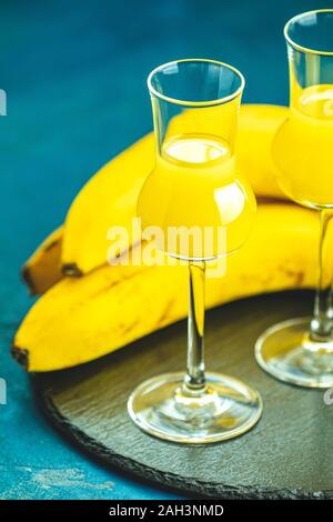 Banana flavoured liqueurs, which French call creme de banana, in grappas wineglass on dark blue concrete surface Stock Photo