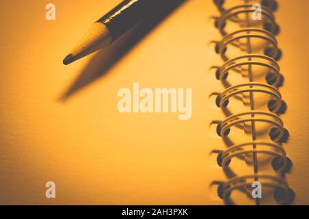 pencil and paper in an open spiral notebook, closeup photo, yellow warm tone. Stock Photo
