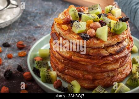 Pancakes with honey, kiwi, nuts and raisins are on the table Stock Photo