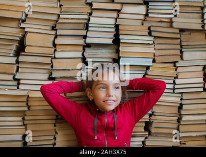 Little smiling schoolgirl over bookshelf background. Knowledge concept. Stock Photo