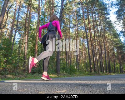 Side-back view of a running woman in wooded forest. Fitness healthy lifestyle concept. Stock Photo
