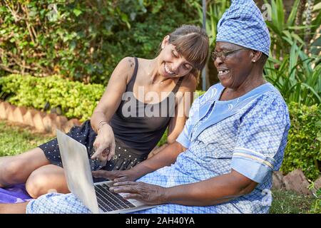 Happy senior woman sitting on lawn sharing laptop with a woman Stock Photo
