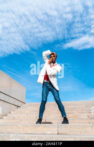 Young man standing on stairs outdoors with hands on face Stock Photo